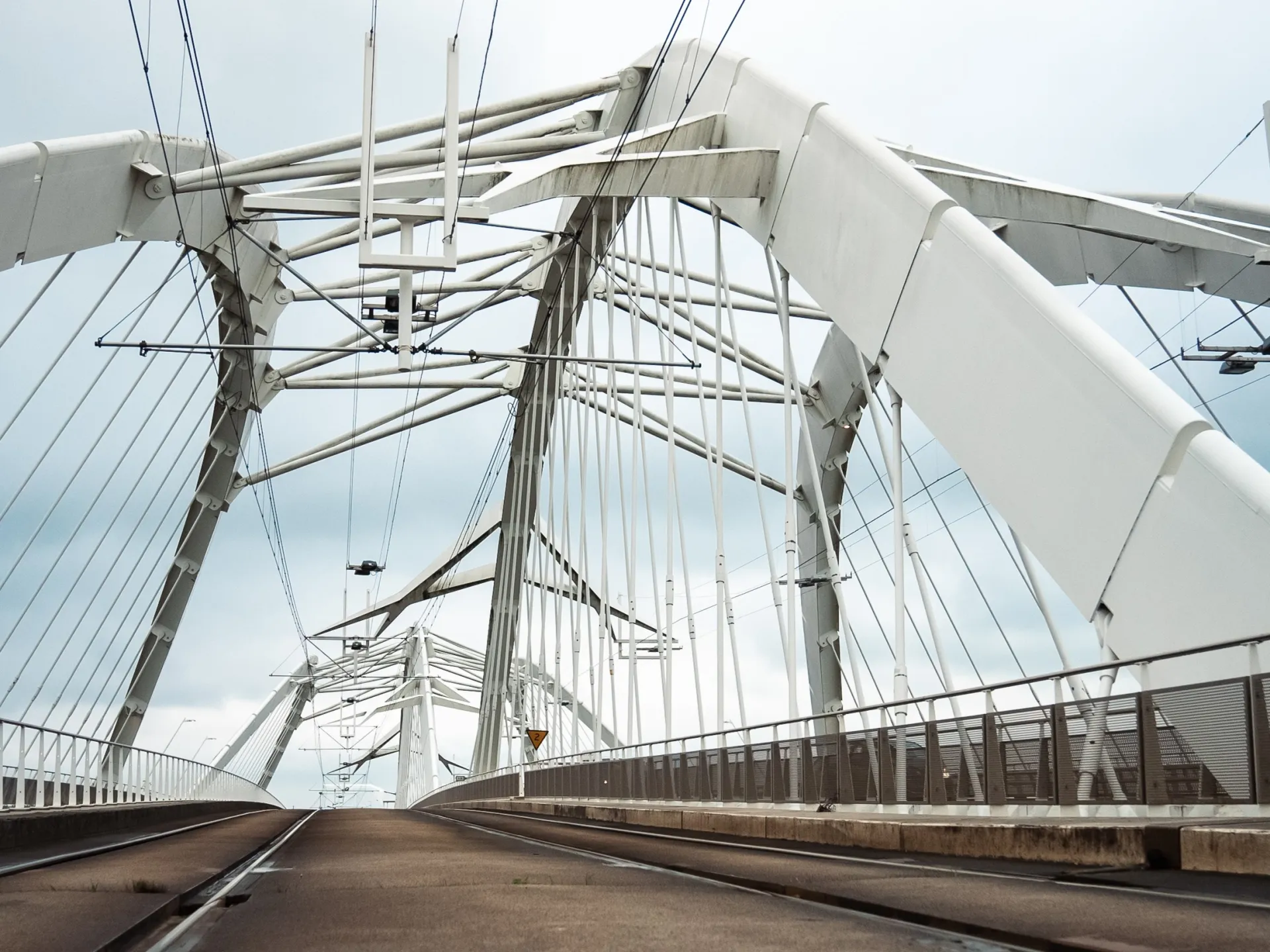 Witte stalen boogbrug met tram- en spoorbaan, gezien vanaf het wegdek