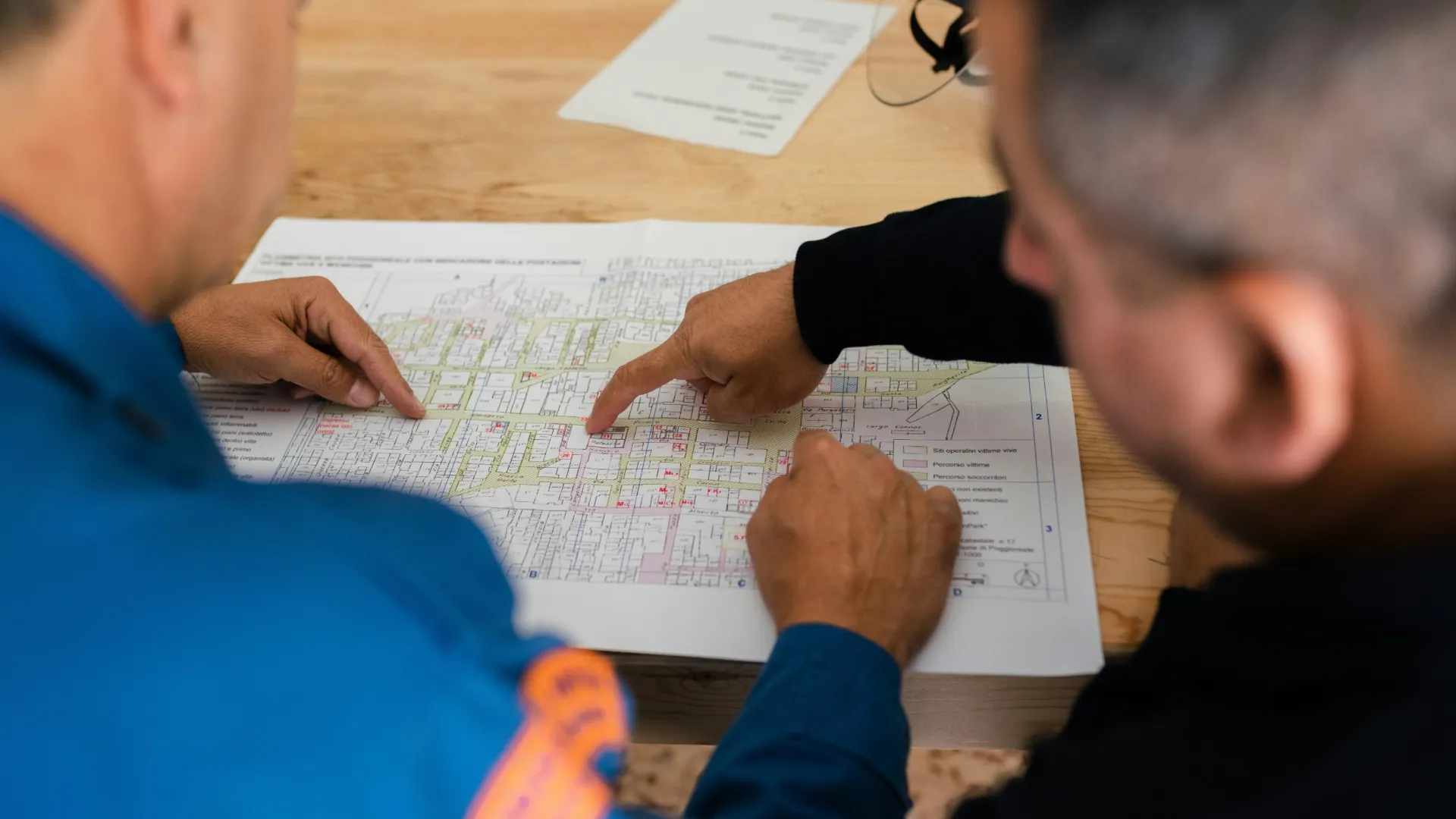 Twee vakmensen wijzen details aan op een plattegrond tijdens een werkoverleg