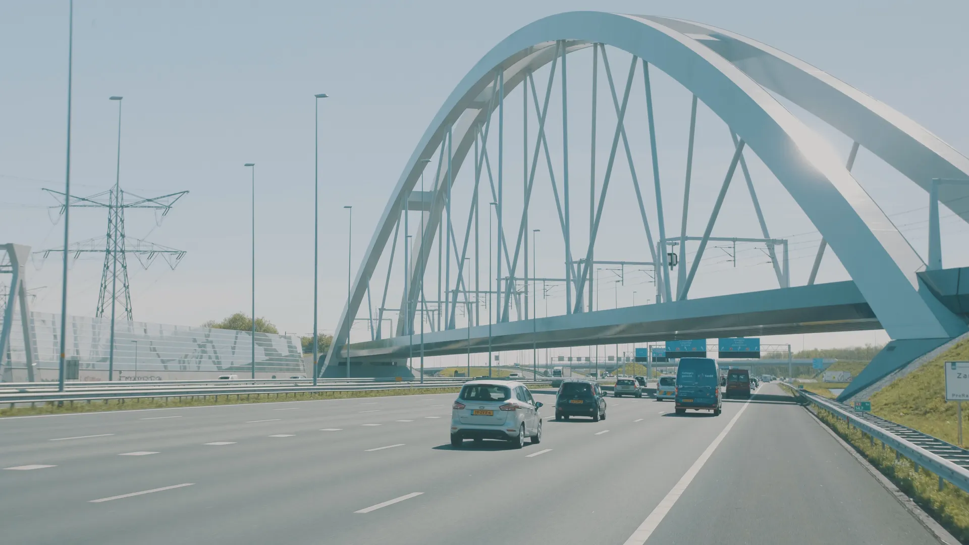 Stalen spoorboogbrug over een Nederlandse snelweg met hoogspanningsmast