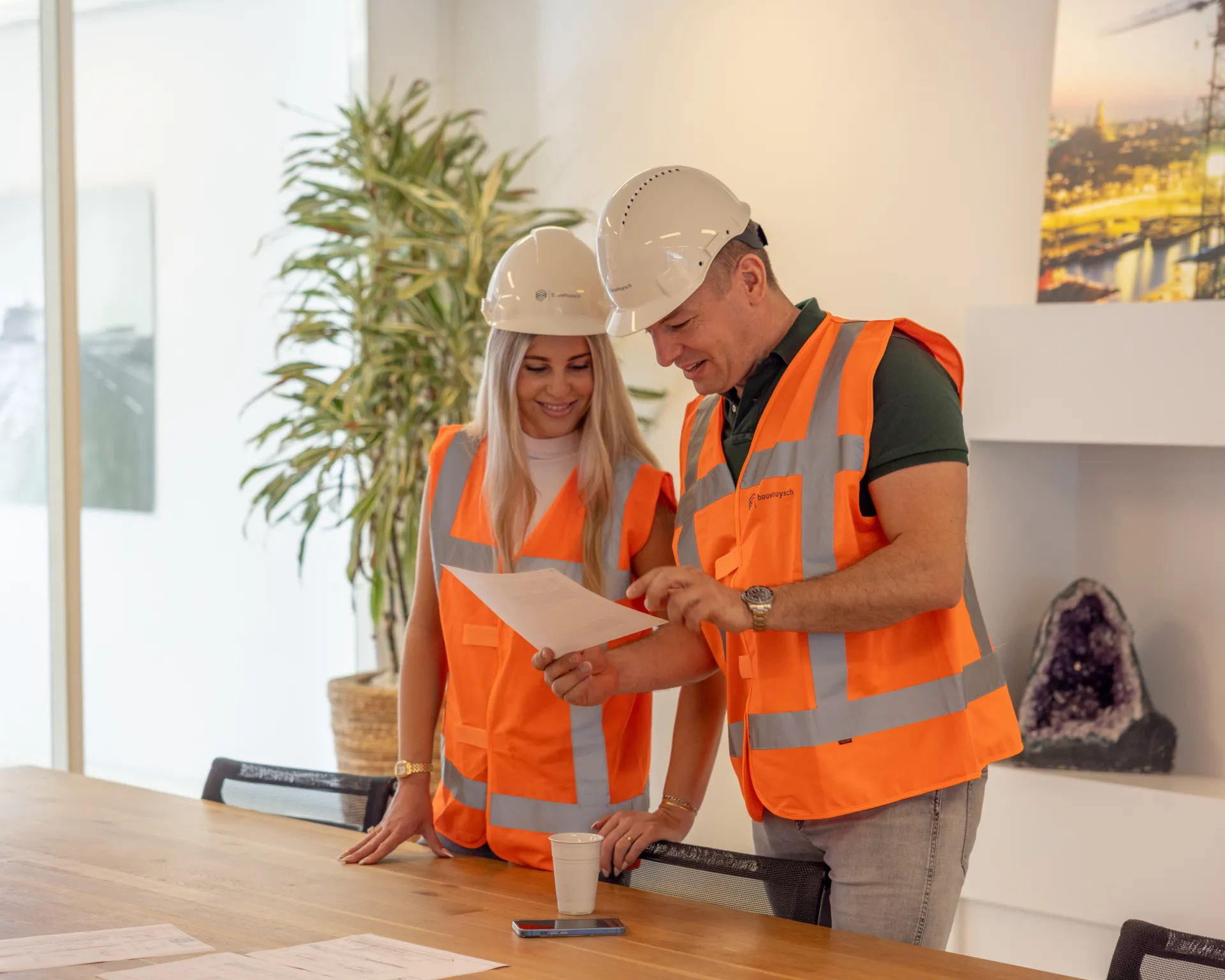 Twee collega's van Bouwhuysch met helm en veiligheidshesje bespreken een bouwtekening