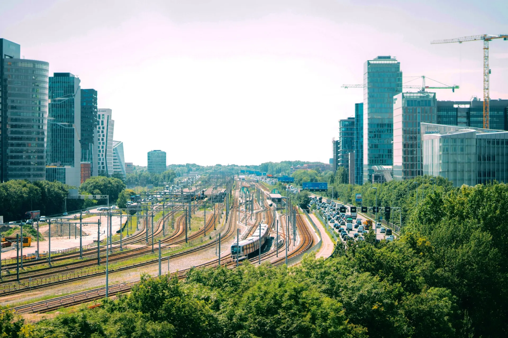 Sporen, snelweg en hoogbouw in de Amsterdamse Zuidas met bouwkranen aan de horizon