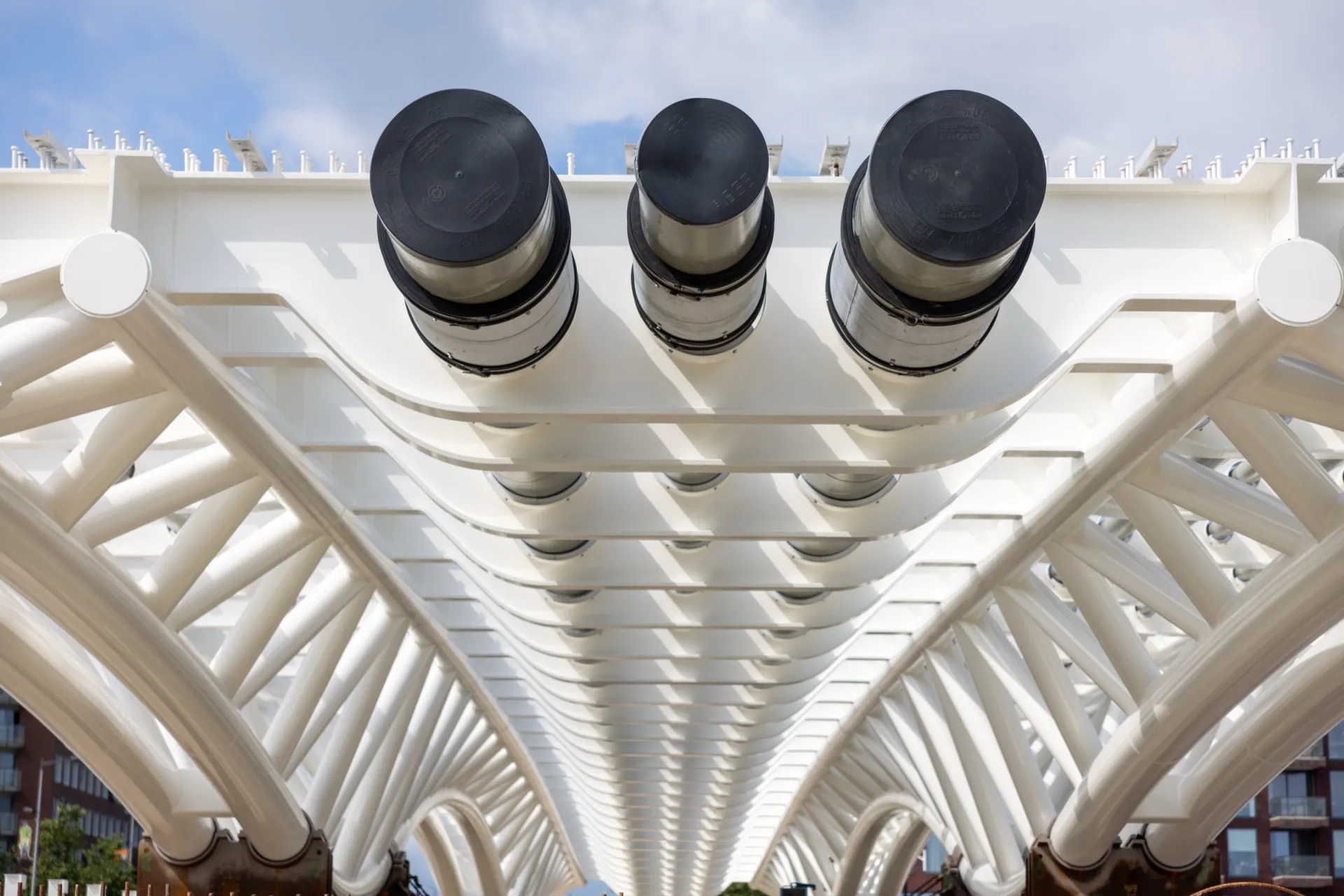 Onderaanzicht van een witte leidingbrug met rijen gebundelde leidingen